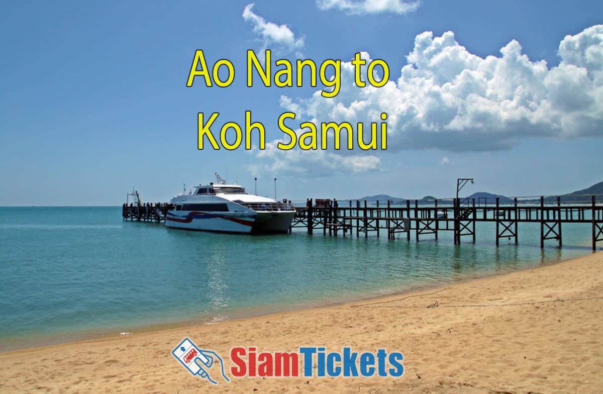 A blue and white Lomprayah catamaran docked at a wooden pier on a sandy beach under a clear blue sky with puffy white clouds.