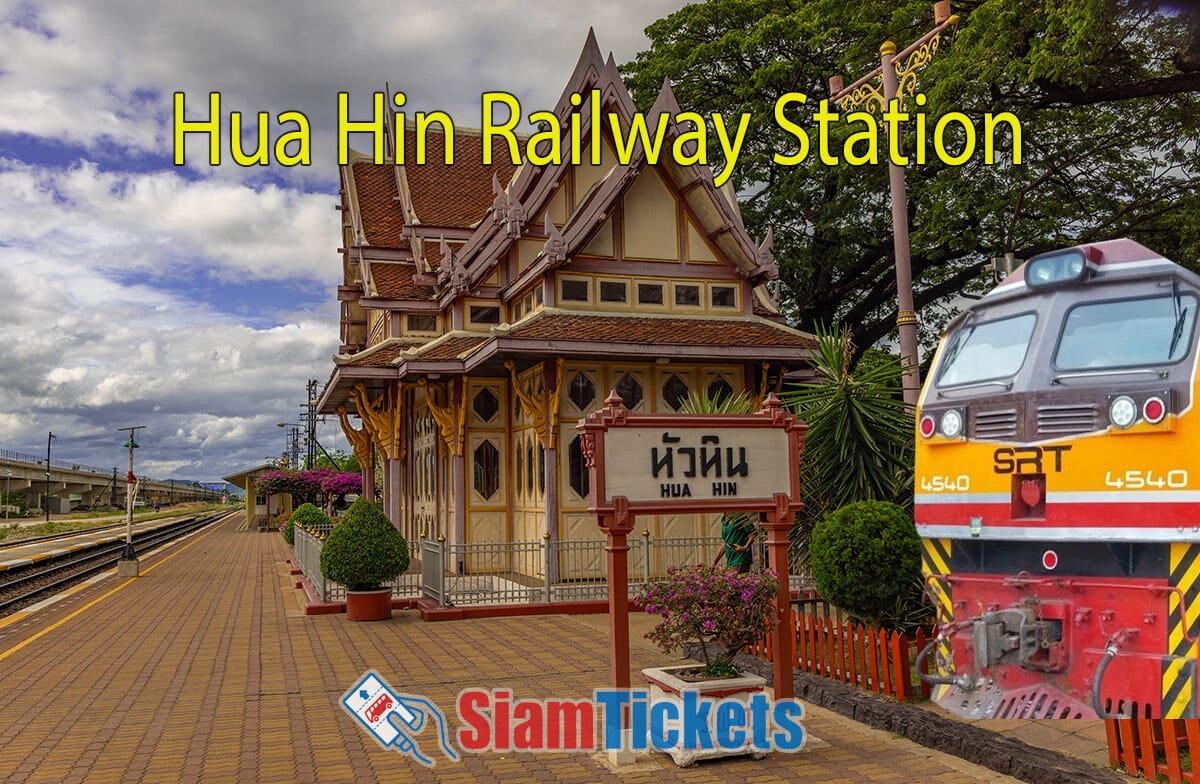 Vibrant view of Hua Hin Railway Station in Thailand, showcasing its traditional Thai architecture and a colorful SRT train approaching the platform. The station is adorned with intricate wooden designs and surrounded by lush greenery.