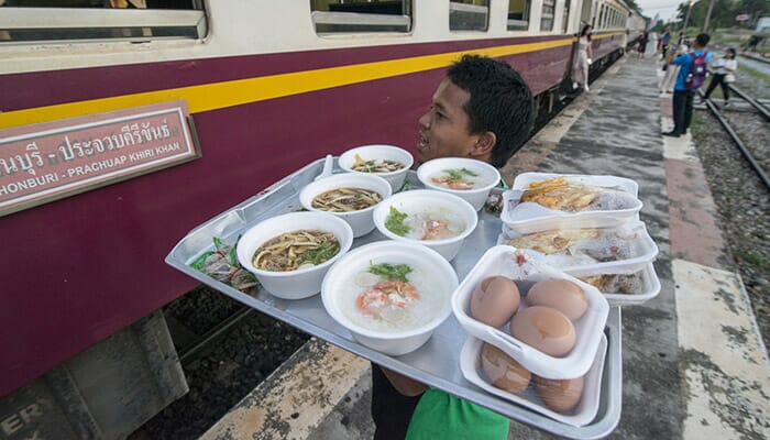 Thai train food vendor offering local dishes to passengers through train window